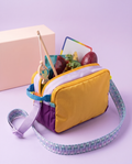 The Analog Bag, Customised, in Purple and Yellow, open with a wooden fishing rod, magnetic tiles, a dinosaur, a wipe-off board and a cork-foam egg packed inside, gift box behind