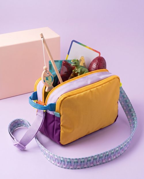The Analog Bag, Customised, in Purple and Yellow, open with a wooden fishing rod, magnetic tiles, a dinosaur, a wipe-off board and a cork-foam egg packed inside, gift box behind